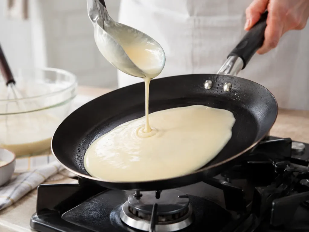 Pfannkuchenteig wird in einer Pfanne zu einem dünnen Pfannkuchen gebacken